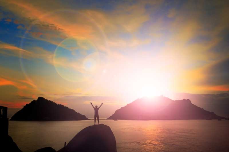 Photo of man on rock near ocean at sunset.