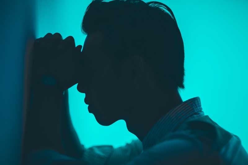 Photo of man in pain leaning against a wall.